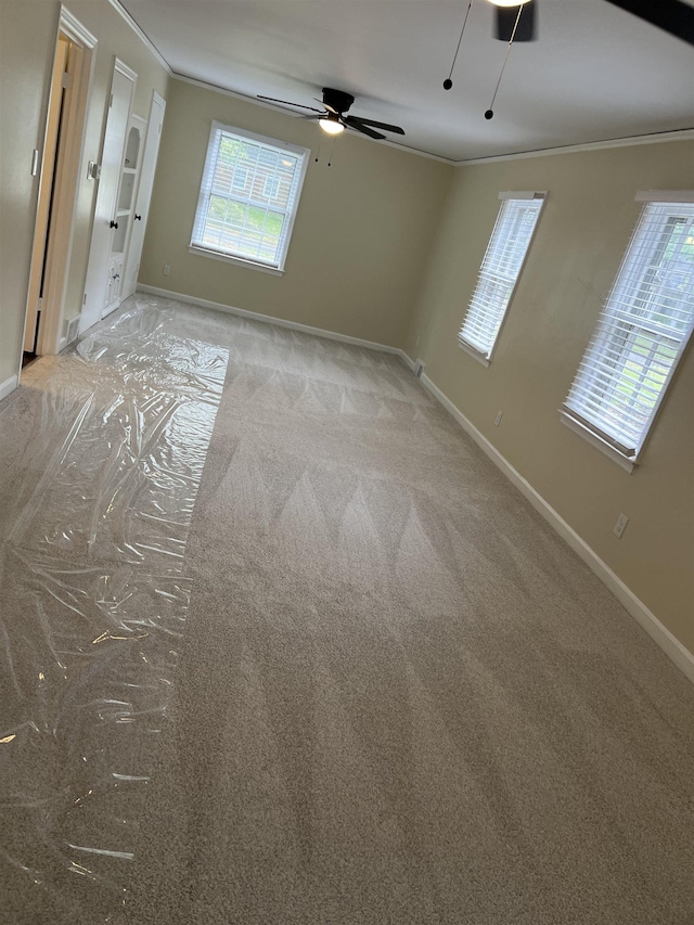 empty room with ornamental molding, baseboards, a ceiling fan, and light carpet