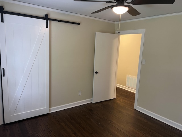 unfurnished bedroom with a barn door, dark wood-type flooring, crown molding, baseboards, and ceiling fan