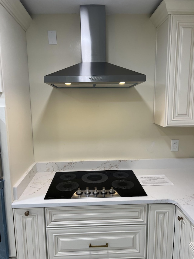 kitchen view of wall chimney range hood, black electric cooktop, and white cabinetry
