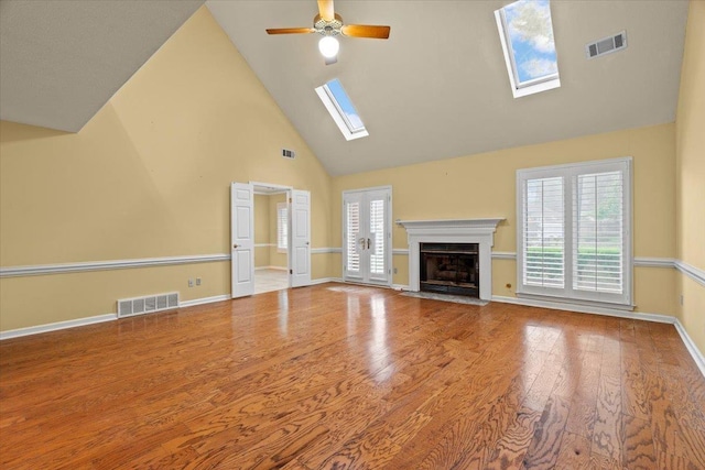 unfurnished living room with visible vents, a skylight, wood finished floors, and high vaulted ceiling