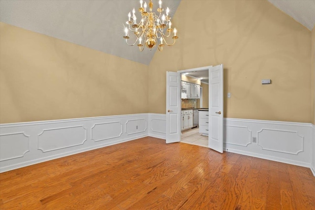 unfurnished dining area featuring a notable chandelier, wainscoting, light wood-style flooring, and lofted ceiling