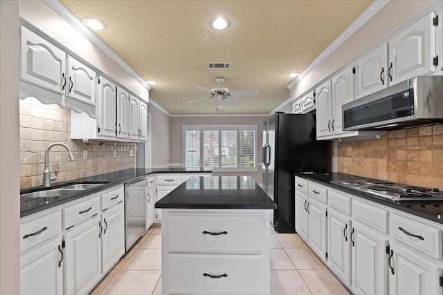 kitchen with appliances with stainless steel finishes, dark countertops, a sink, visible vents, and crown molding