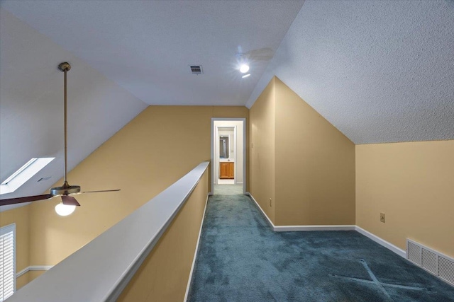 corridor with lofted ceiling with skylight, visible vents, dark colored carpet, and baseboards