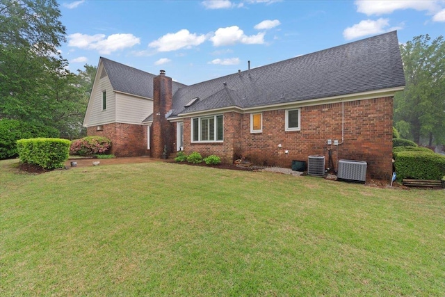 back of property featuring brick siding, a yard, central AC unit, and a chimney