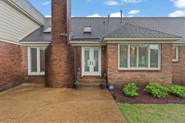 back of property featuring a patio, a chimney, brick siding, roof with shingles, and french doors