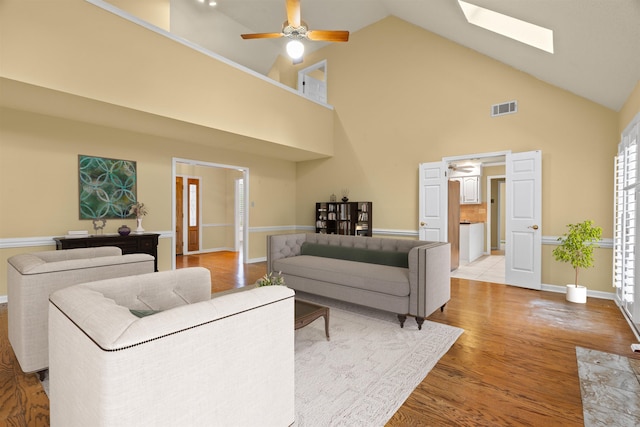 living area with light wood finished floors, high vaulted ceiling, a ceiling fan, visible vents, and a skylight