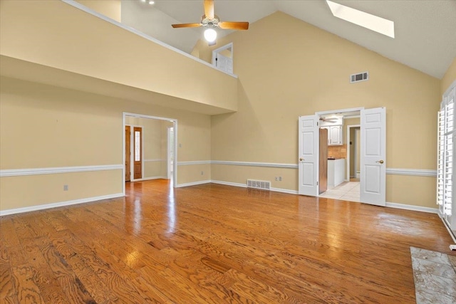 unfurnished living room with visible vents, a ceiling fan, high vaulted ceiling, and a skylight