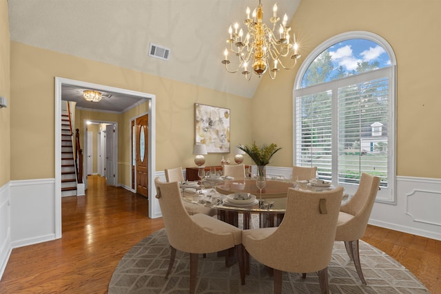dining space with wood finished floors, stairway, a chandelier, a wainscoted wall, and visible vents