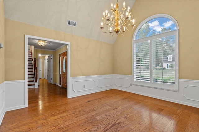 unfurnished dining area featuring wood finished floors, a chandelier, vaulted ceiling, a wainscoted wall, and visible vents