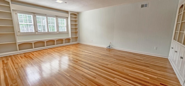spare room with visible vents, wood finished floors, built in shelves, and a textured ceiling