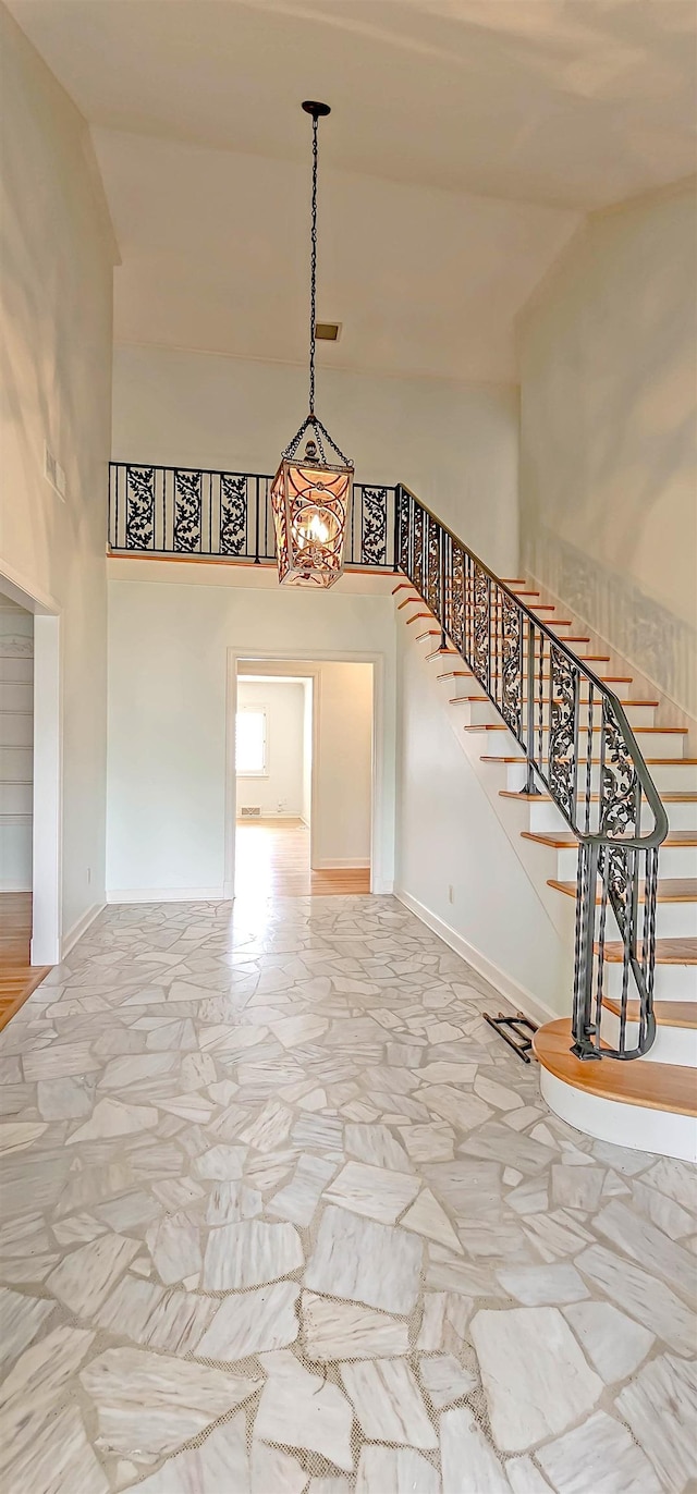 interior space with stone flooring, high vaulted ceiling, a chandelier, and baseboards