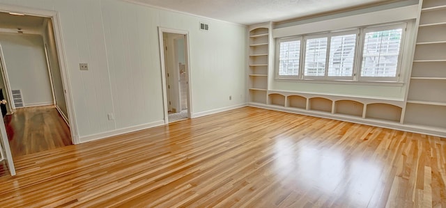 unfurnished room with crown molding, visible vents, wood finished floors, and baseboards