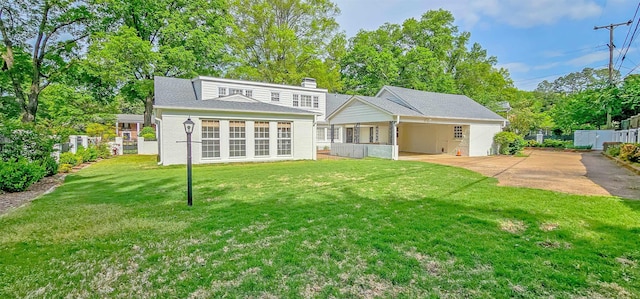 back of property with a chimney, brick siding, fence, concrete driveway, and a lawn