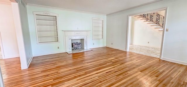 unfurnished living room with light wood-style floors, built in features, ornamental molding, a premium fireplace, and stairway