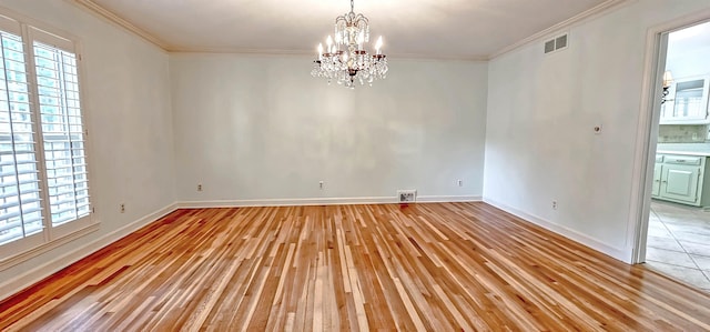 empty room featuring a chandelier, light wood-type flooring, visible vents, and ornamental molding