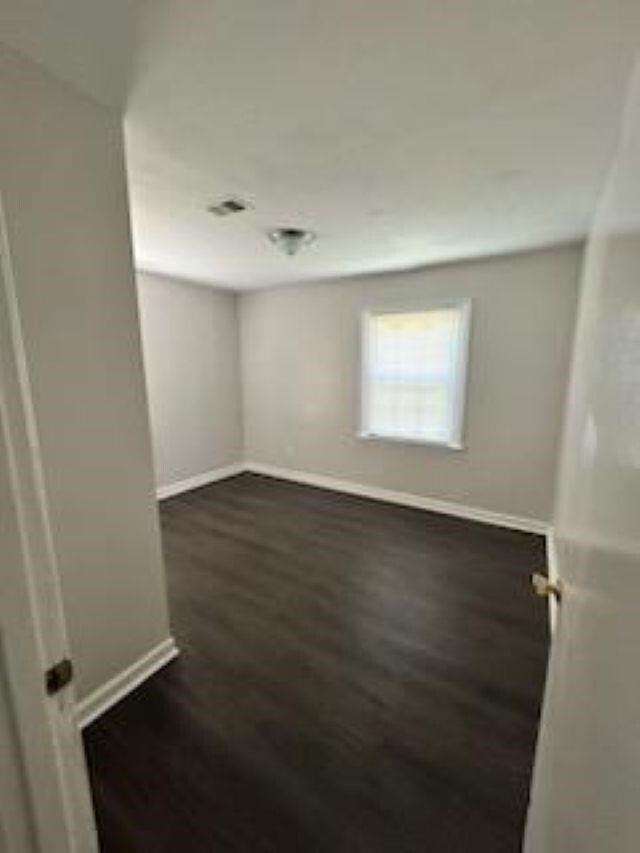 spare room featuring dark wood-style flooring and baseboards