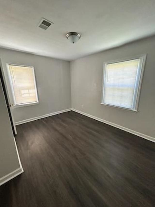 unfurnished bedroom with multiple windows, visible vents, dark wood finished floors, and baseboards