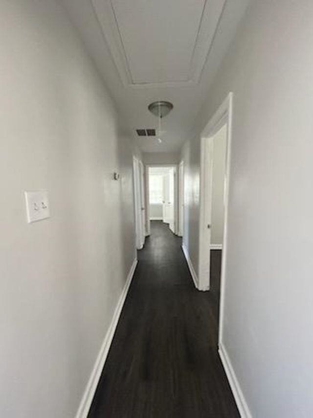 hallway with attic access, dark wood-type flooring, visible vents, and baseboards