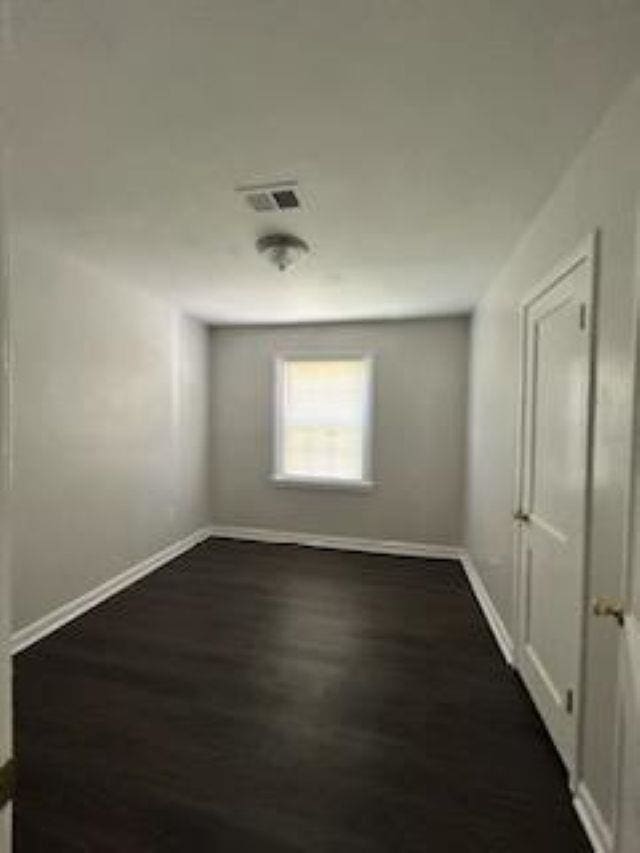 unfurnished room featuring baseboards, visible vents, and dark wood-style flooring