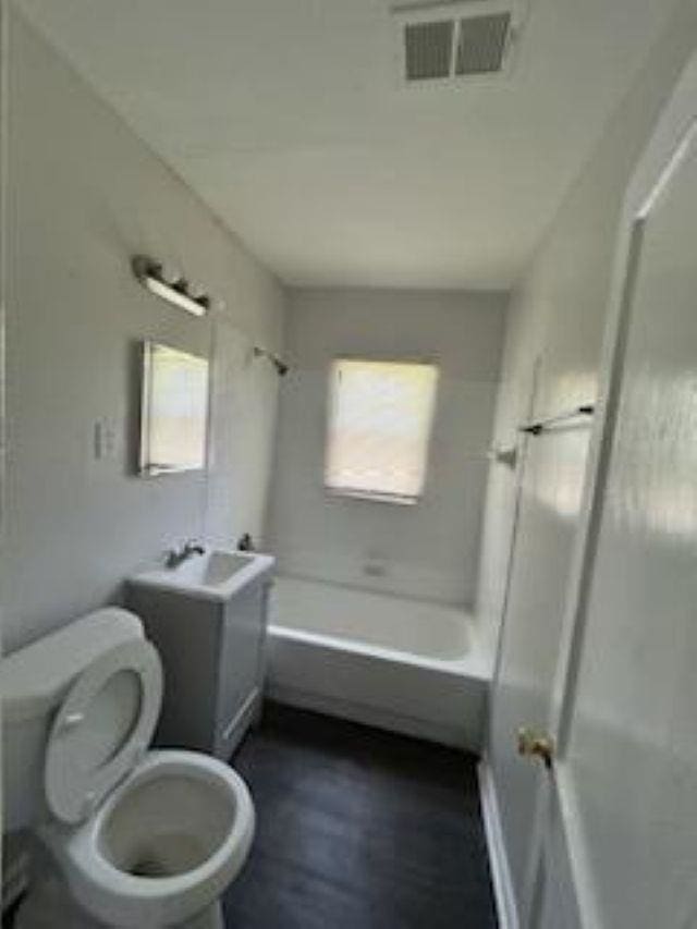 bathroom featuring wood finished floors, toilet, a sink, visible vents, and tub / shower combination