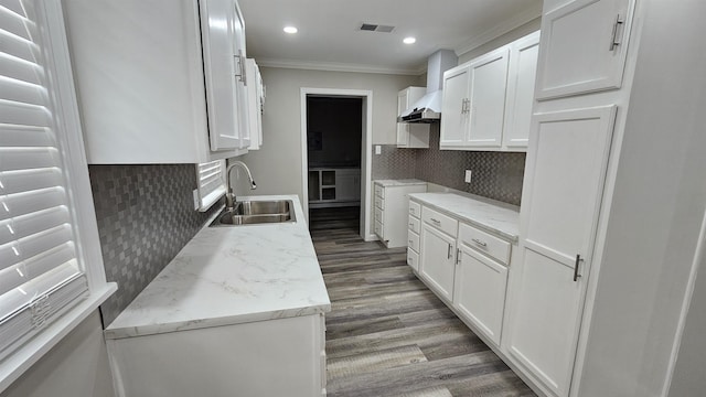 kitchen featuring visible vents, crown molding, wood finished floors, a sink, and wall chimney exhaust hood