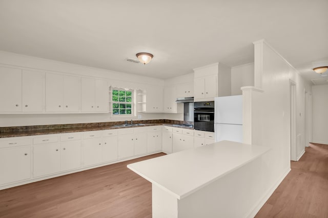 kitchen featuring under cabinet range hood, light wood-type flooring, visible vents, black oven, and freestanding refrigerator