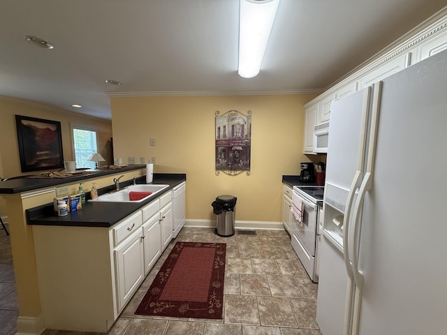 kitchen featuring white cabinetry, a sink, dark countertops, white appliances, and a peninsula