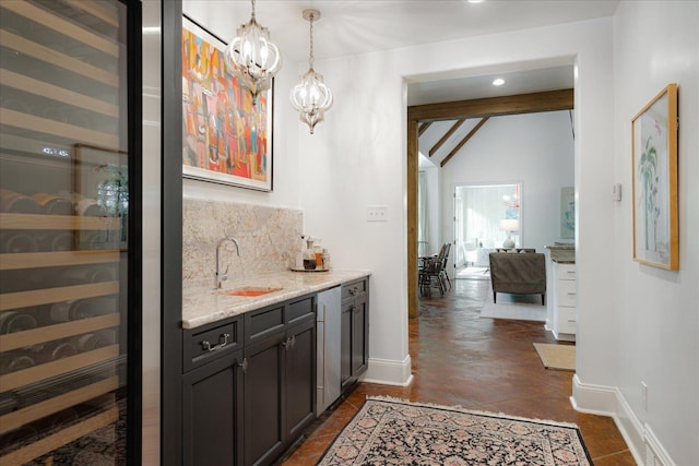bar with a sink, baseboards, indoor wet bar, a notable chandelier, and backsplash