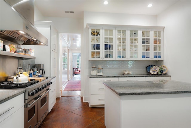 kitchen with dark stone countertops, range with two ovens, visible vents, backsplash, and extractor fan