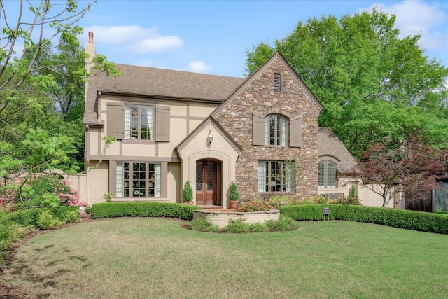 tudor house featuring a chimney, stucco siding, a front yard, and stone siding