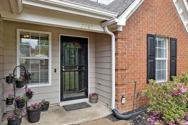 entrance to property featuring roof with shingles and brick siding