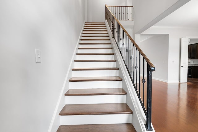 staircase with baseboards, wood finished floors, a high ceiling, and ornamental molding