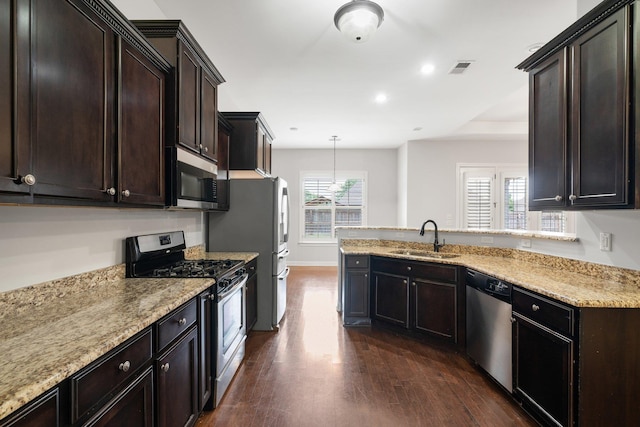 kitchen featuring a peninsula, a sink, appliances with stainless steel finishes, and dark wood-type flooring