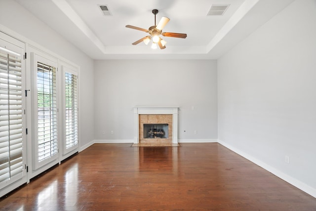unfurnished living room with visible vents, a tray ceiling, a fireplace, wood finished floors, and a ceiling fan