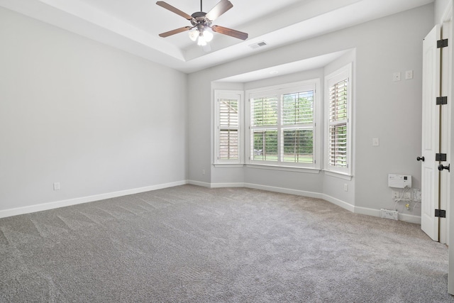 carpeted spare room with visible vents, ceiling fan, a raised ceiling, and baseboards