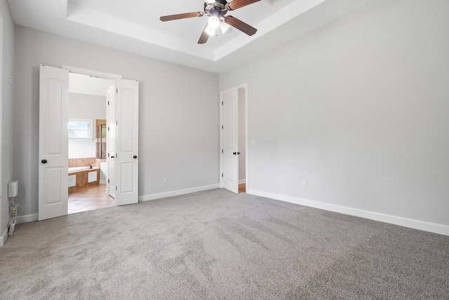 unfurnished bedroom with baseboards, connected bathroom, carpet flooring, and a tray ceiling