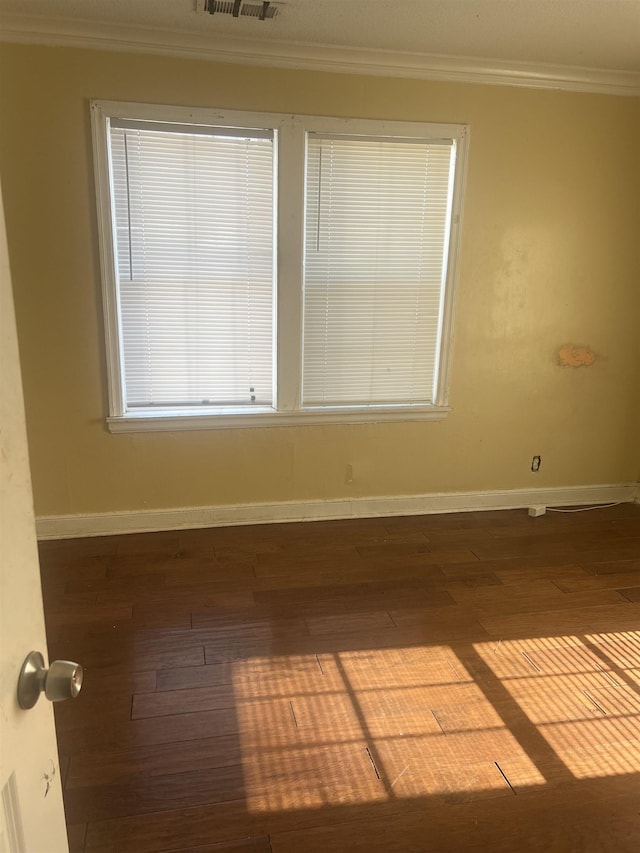 unfurnished room with dark wood finished floors, baseboards, visible vents, and crown molding