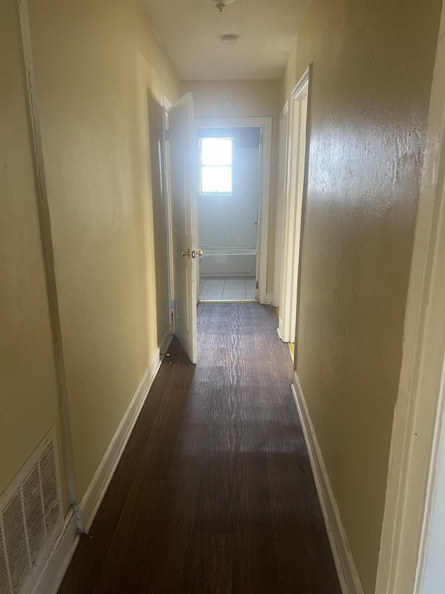 hallway with dark wood-style floors, visible vents, and baseboards