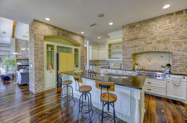 kitchen with dark countertops, stainless steel gas stovetop, visible vents, freestanding refrigerator, and a fireplace