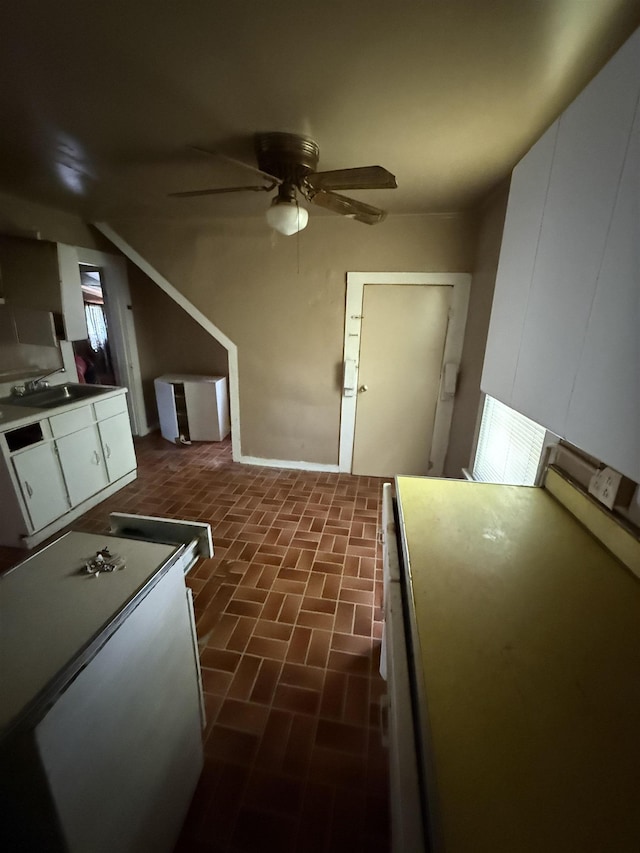 interior space featuring a ceiling fan, white cabinets, brick floor, and a sink