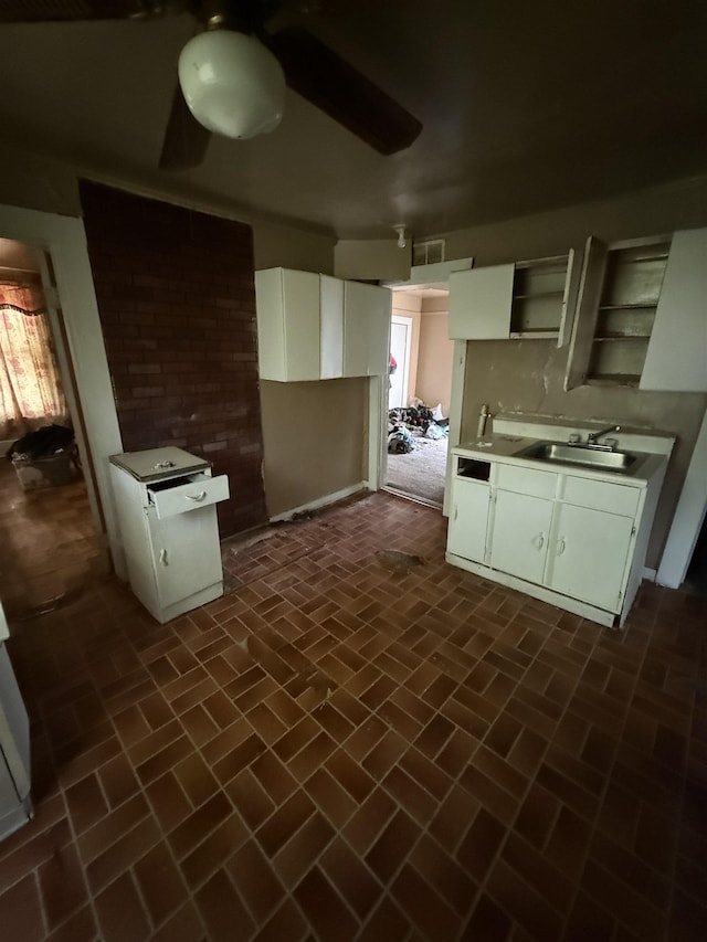 kitchen featuring open shelves, brick floor, light countertops, a sink, and white cabinetry