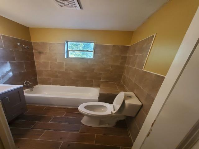 bathroom with washtub / shower combination, visible vents, toilet, tile walls, and vanity