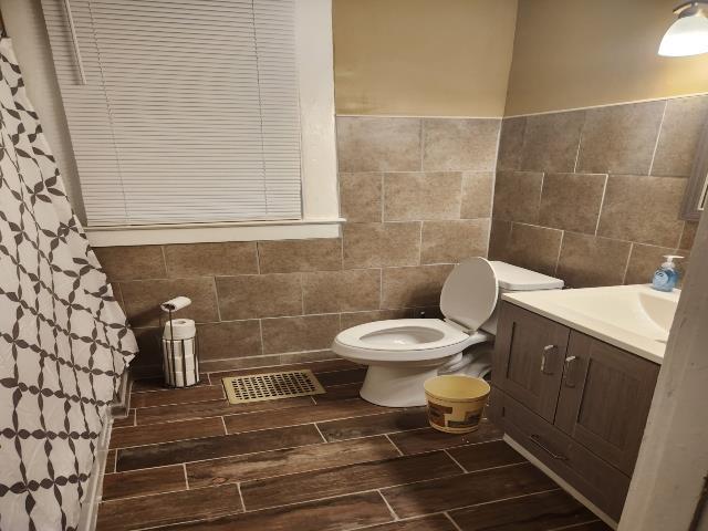 full bath with toilet, tile walls, visible vents, and vanity
