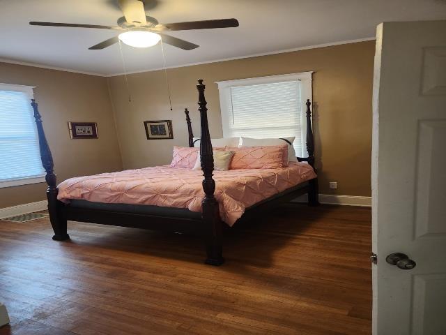 bedroom with wood finished floors, crown molding, a ceiling fan, and baseboards