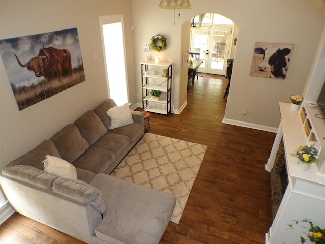 living room with dark wood-type flooring, baseboards, and arched walkways