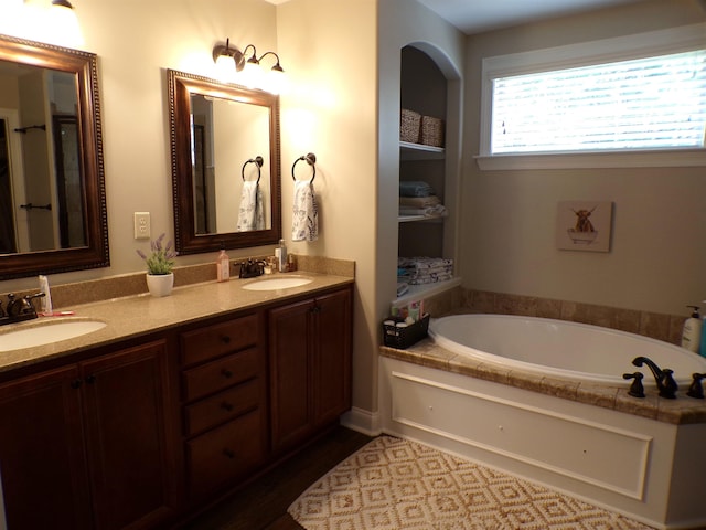 bathroom with a bath, double vanity, a sink, and wood finished floors
