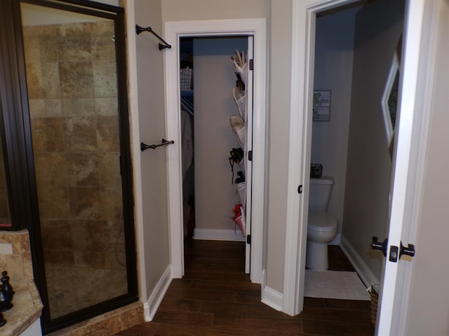 bathroom featuring wood finished floors, a shower stall, toilet, baseboards, and a spacious closet