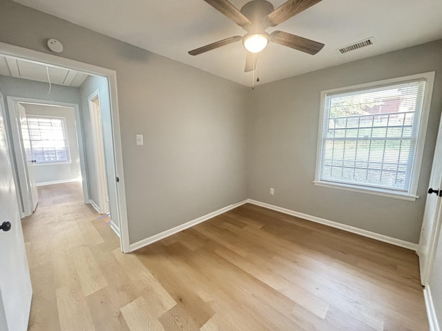 empty room with attic access, a ceiling fan, baseboards, light wood-type flooring, and visible vents
