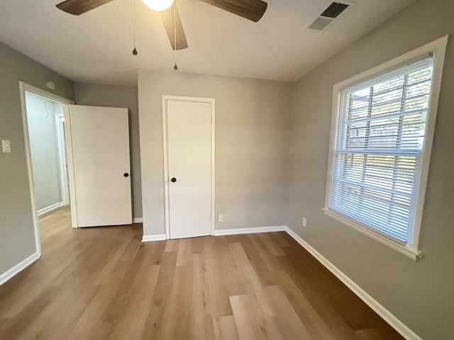 unfurnished bedroom featuring baseboards, visible vents, multiple windows, and wood finished floors