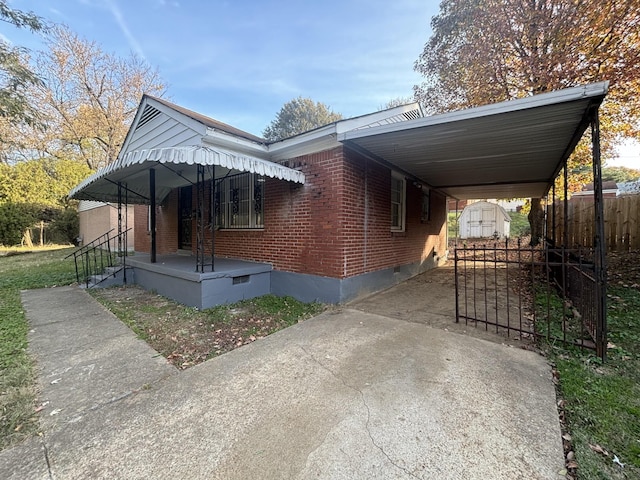 view of front of house featuring a carport, brick siding, fence, a storage unit, and concrete driveway